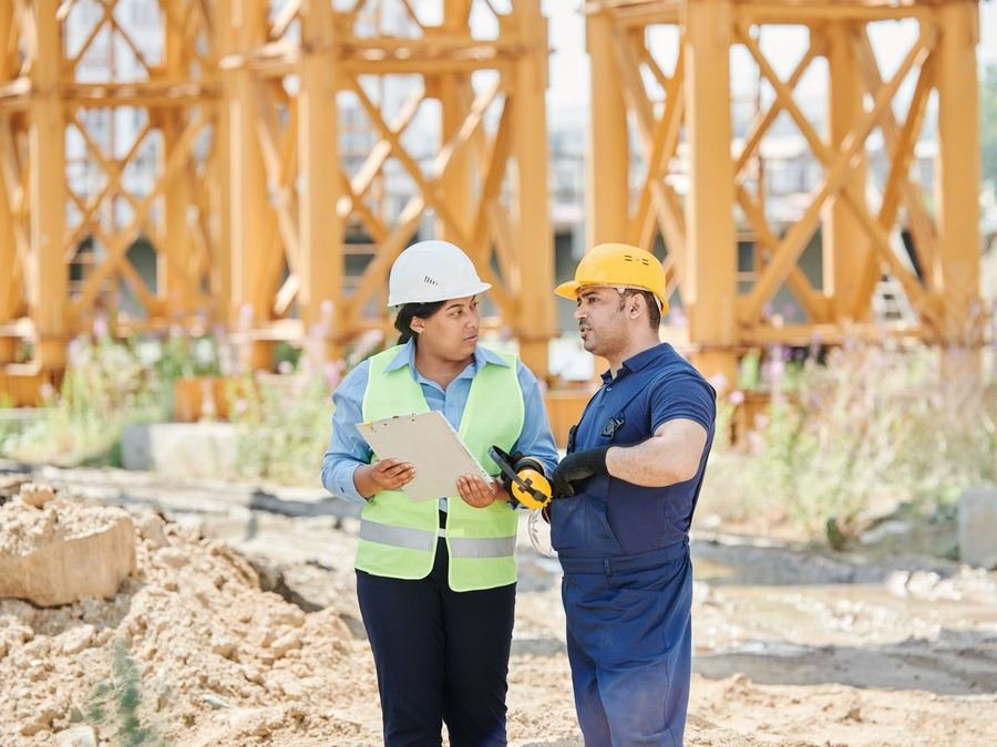 A site engineer with a clipboard talking to a construction worker in overalls on a building site
